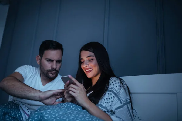 A young man is protesting against his better half using the phone in bed.