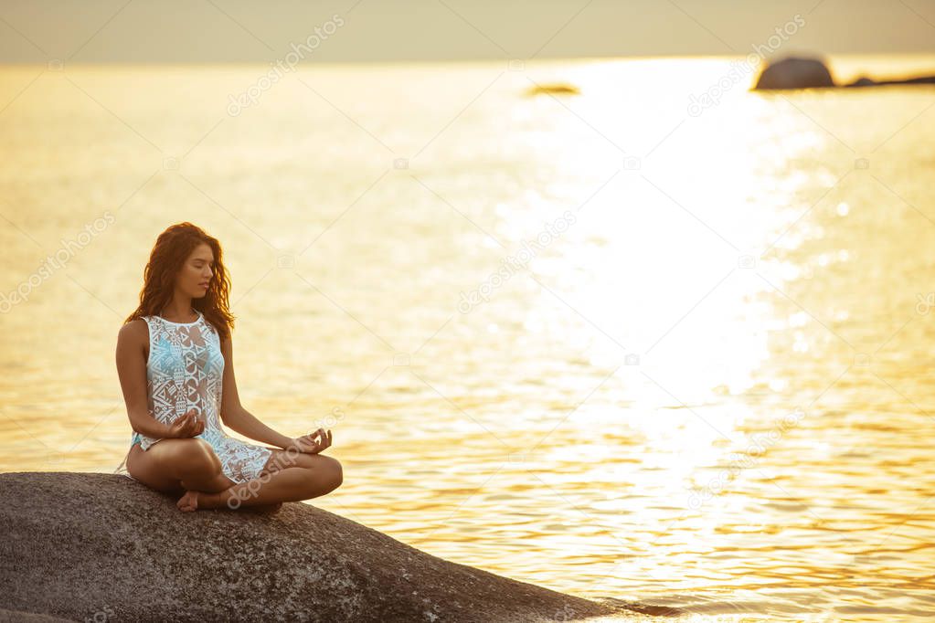 Woman meditating next to the sea on a sunset.