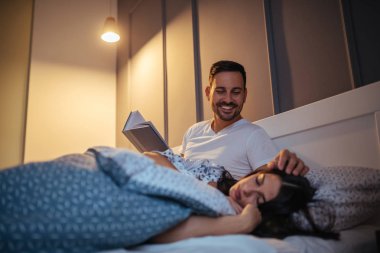 Kız uykuda olduğu gibi genç bir adam yatakta bir kitap okuyor.