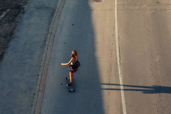 一个年轻美丽的女孩在空荡荡的街道上骑着她的长板 — 图库照片