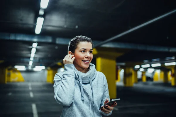 Tiro Uma Mulher Atleta Sorridente Usando Telefone Celular Estacionamento Subterrâneo — Fotografia de Stock