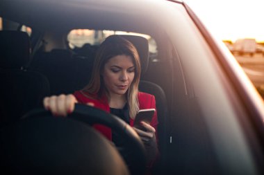 Telefonunu tarama yaparken arabada oturan genç bir profesyonel giyimli kadın.