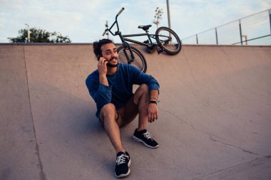 Bmx bisiklet üzerinde yapan bir mola sırasında telefonda konuşurken bir kentsel delikanlı.