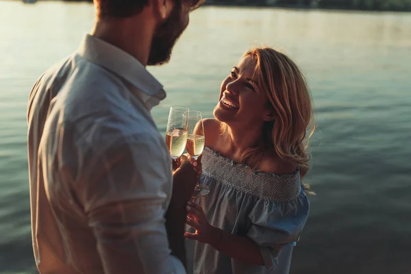 Smiling young couple toasting with wine outdoors at sunset.