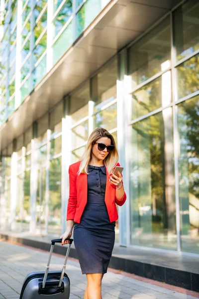 Beautiful young  businesswoman pulling a suitcase and using mobile phone.