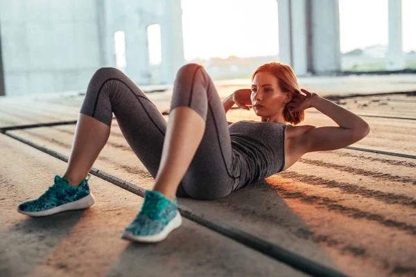 A young athletic woman doing sit ups in an urban area.