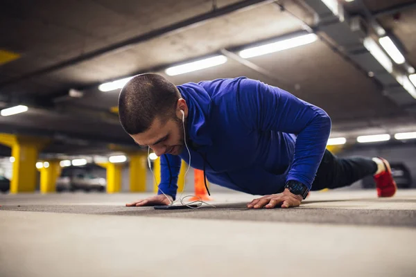 Joven Haciendo Flexiones Dentro Garaje Urbano Mientras Escucha Música Teléfono — Foto de Stock