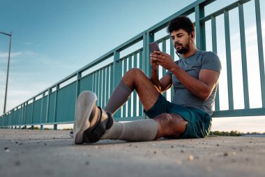 Telefonunu kullanarak yerde oturan genç adam