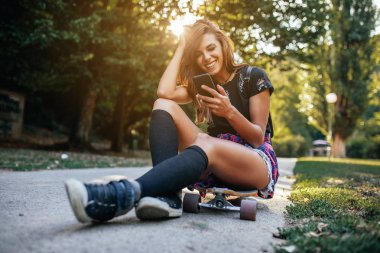 Bir cep telefonu tutarak uzun bir tahta üzerinde oturan genç kız