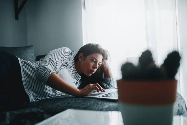 A young woman is lying down on her couch and watching her favorite movie online.