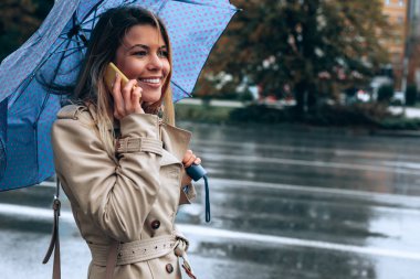 Güzel bir genç kadın mutlu biriyle son derece yağışlı hava altında telefonunda çok özel konuşuyor.