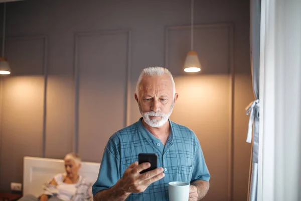 Uomo Anziano Con Cellulare Mano Sua Moglie Background Sdraiato Letto — Foto Stock