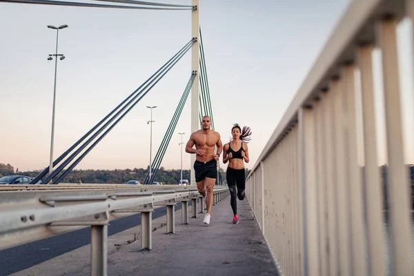 年轻的肌肉发达的夫妇在桥上慢跑 — 图库照片