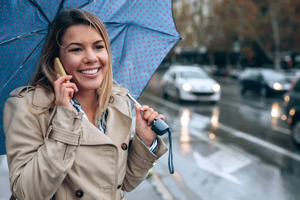 Молода Усміхнена Жінка Стоїть Посеред Вулиці Під Парасолькою Розмовляє Телефону — стокове фото