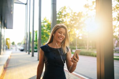 Zarif bir genç kadın müzik dinlerken sokağın yürüyor.