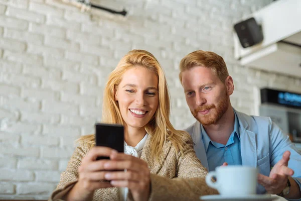 若い男性と女性は笑みを浮かべて携帯電話を見て — ストック写真