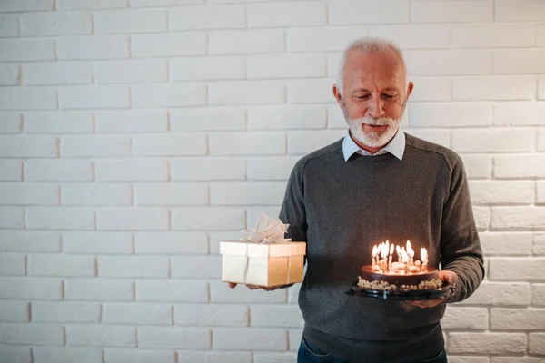 Elderly man holding a birthday cake and a present