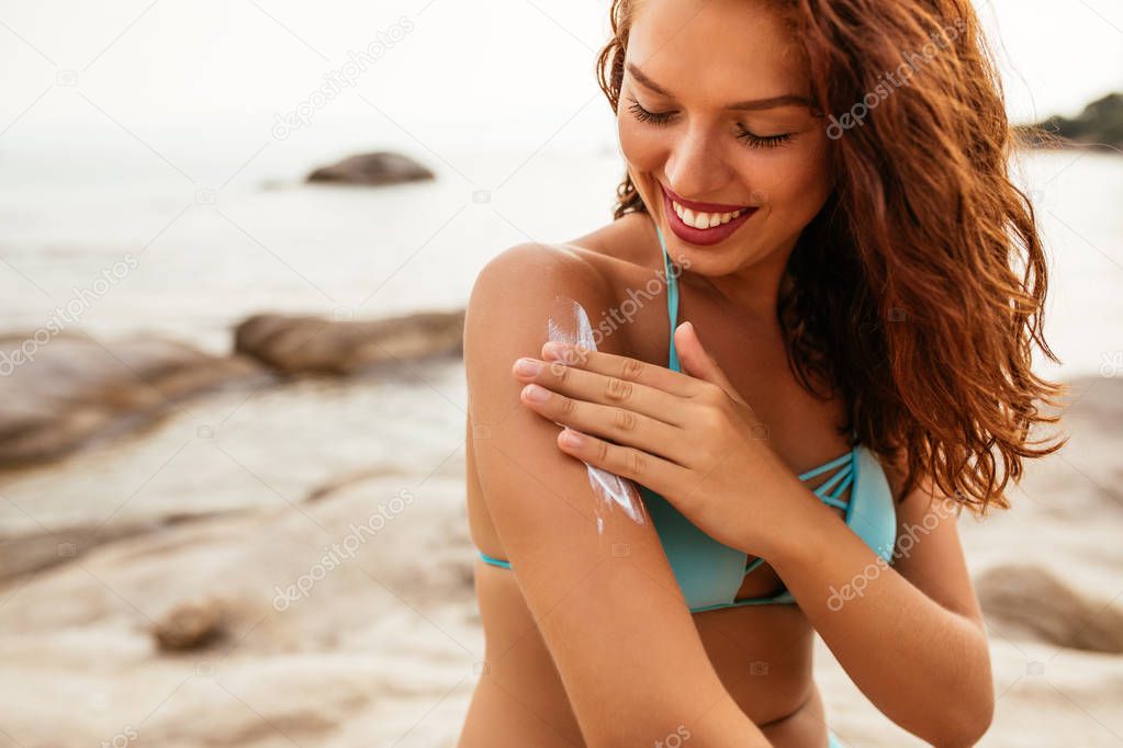 Young woman applying sunscreen lotion on the beach