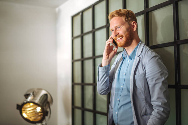 Портрет красивого улыбающегося молодого бизнесмена, разговаривающего по мобильному телефону
.