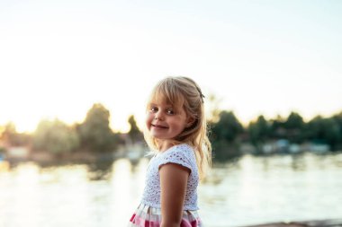 Nehir kenarında gülümseyen bir sarışın küçük kız portresi.
