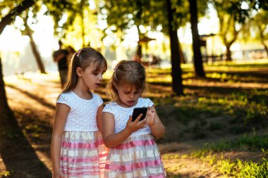 İki kız kardeşi doğarken parkta cep telefonu bakarak portresi.