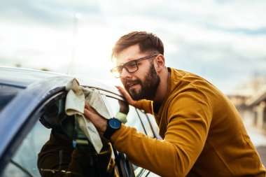 Genç bir adamın arabasını mikrofiber bezle dikkatlice temizlik atış.