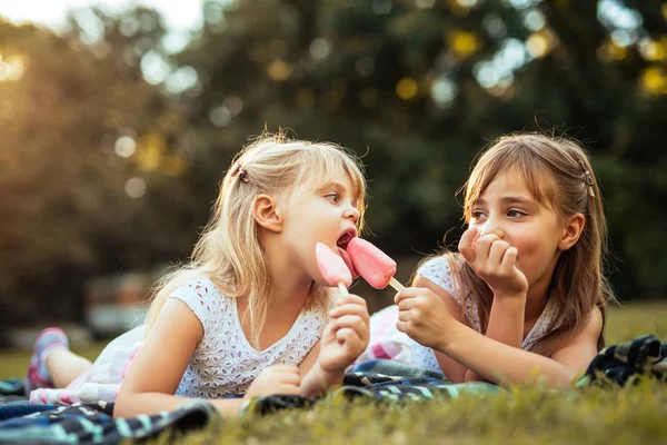 Shot of two blonde sisters eating ice cream on a picnic in the park.