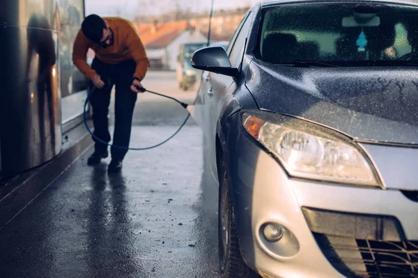 ノズルを屋外で自分の車を洗う若い男のショット — ストック写真