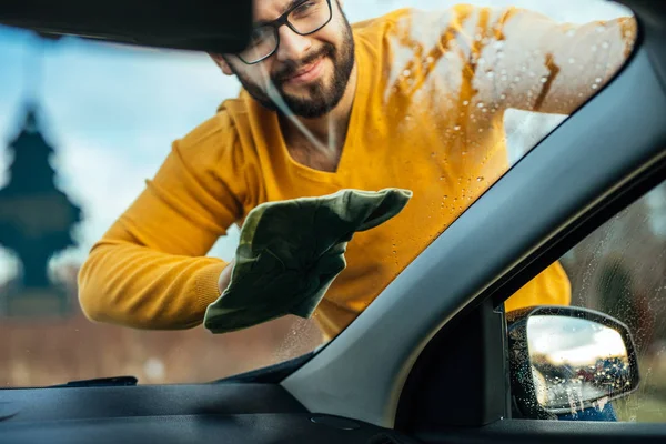 若い男が彼の車の窓から外のマイクロファイバーの布で研磨のショット — ストック写真