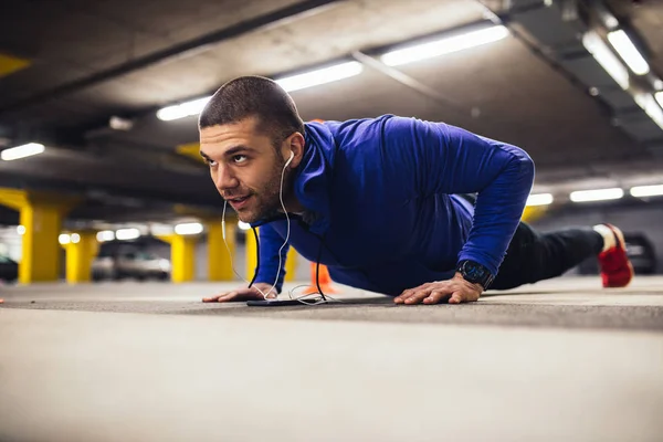 Shot of an athlete man doing pushups and listening to the music underground.