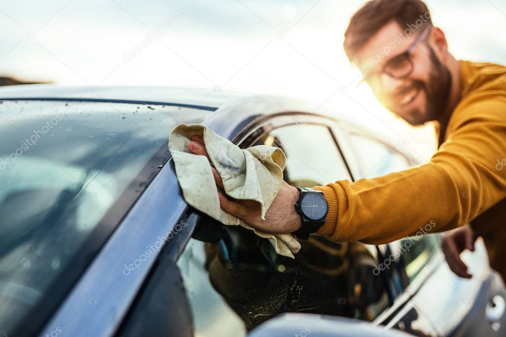 Shot of a happy young man polishing his car with microfiber cloth.