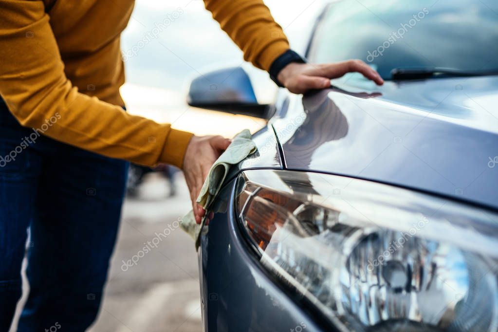 Shot of a male polishing his car with microfiber cloth.