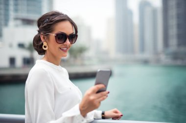 Gülümseyen bir işkadını Nehri yanındaki şehirde bir cep telefonu kullanarak fotoğraf kapatmak.