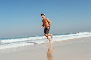 Sahilde sıcak yaz gününde okyanus tarafından çalışan yakışıklı bir genç adam portresi.