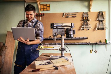 Genç marangoz atölyesini bir dizüstü bilgisayar üzerinde çalışan.
