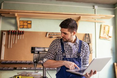 Genç marangoz atölyesinde dizüstü kullanarak portresi.