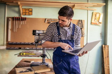Genç marangoz atölyesinde dizüstü kullanarak portresi.