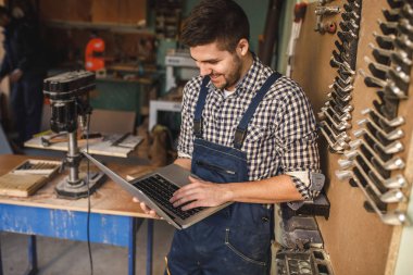 Genç marangoz atölyesini bir dizüstü bilgisayar üzerinde çalışan.
