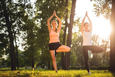 İki kız parkta germe egzersizleri yapıyor.