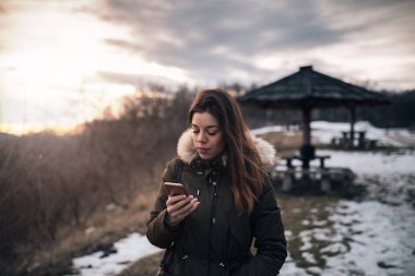 Kış vakti dağda tadını çıkarırken akıllı telefon kullanan güzel kız.