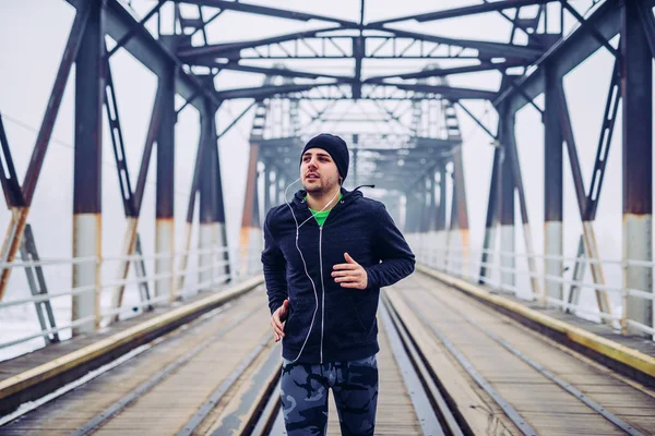 Foto Joven Macho Corriendo Por Puente Escuchando Música Durante Entrenamiento —  Fotos de Stock