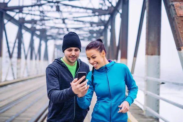 Athletic woman and man having fun with mobile phone on the train bridge on an early morning workout.