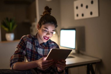 Evde dijital bir tablet üzerinde çalışan bir memnun genç iş kadını portresi.