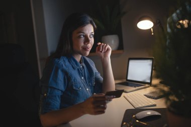 Akşamları evde kredi kartı ile genç gülümseyen bir kadın portresi.