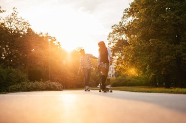 Genç bir çift kaykaylar sokakta günbatımında sürüş tam uzunlukta portresi.