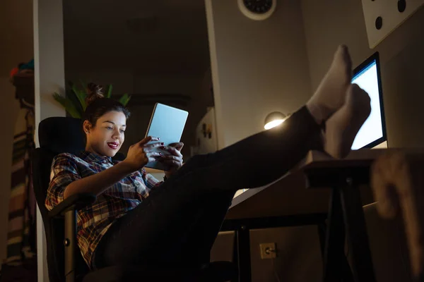 Smiling businesswoman resting at home holding digital tablet late at night.