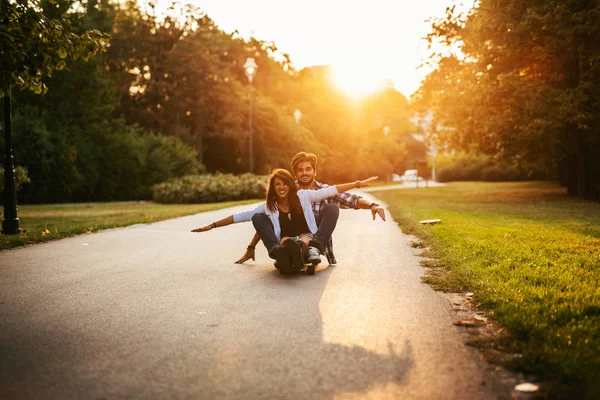 开心快乐微笑的年轻夫妇的照片在日落时分在街上玩滑板 — 图库照片
