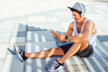 Müzik ve dışında oturan bir gülümseyen genç atletik bir adam çekim.