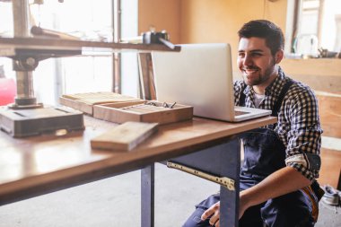Genç marangoz atölyesinde bir dizüstü bilgisayar üzerinde çalışan portresi.