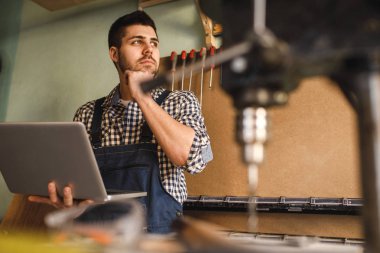 Atış laptop kullanarak gülümseyen bir marangoz atölyesinde çalışmak.